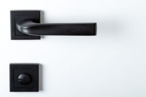 Modern black door handle on white wooden door in interior. Knob close-up elements.