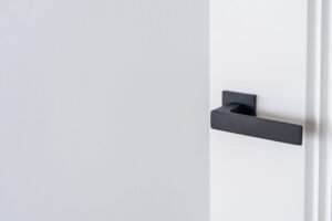 Modern black door handle on white wooden door in interior. Knob close-up elements. Door handle, fittings for interior design. Element of interior design